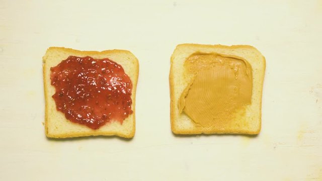 Sandwich with raspberry jam and nut butter on white bread. Hands of a teenager raise a sandwich from the table. Time-laps