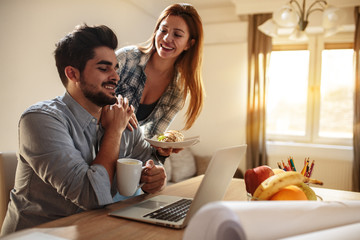 Young married couple sitting on bed at home and using laptop.