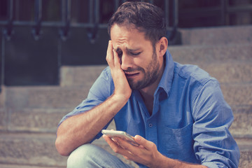 Upset man looking at his mobile phone outdoors