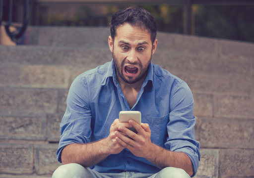Shocked man looking at mobile phone seeing bad news or reading text message