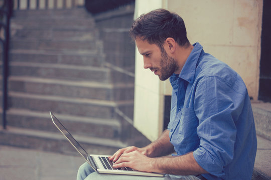 man working on laptop outdoors sitting on steps outside of his office