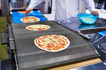 Worker cook adds cheese to pizza on conveyor
