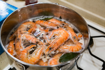 Giant tiger shrimps with heads are cooked with a laurel leaf in a saucepan on a gas stove