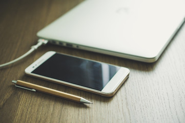 Pencil with smartphone and blur laptop charging battery vintage tone background