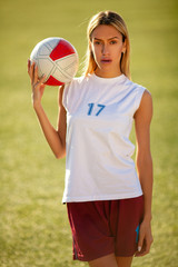 Girl in soccer uniform standing on football field with ball.