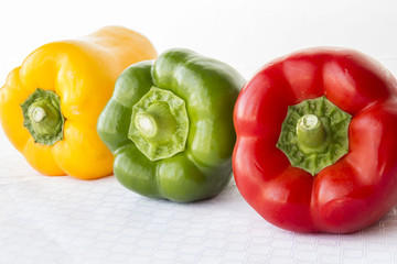 horizontal image of a red and green and yellow peppers lying in a row at an angle on white background.