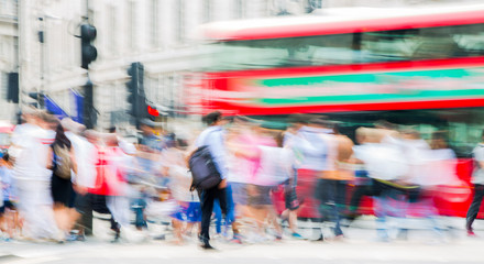 Piccadilly circus with lots of people, tourists and Londoners crossing the junction. Red bus at the background. Blurred type image