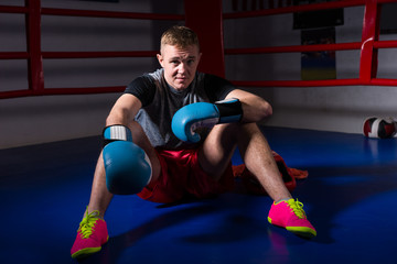 Fototapeta na wymiar Sporty male boxer in boxing gloves sitting in regular boxing ring