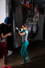 Female boxer in boxing gloves training with her trainer and boxing punching bag