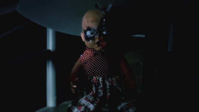A scary haunted doll, eyes burned, looking at the viewer. Handheld travelling shot.  Halloween horror themed clip.
