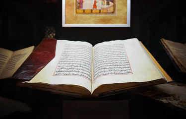 Святая Исламская старая книга Коран открыт в кожаной обложке на фоне других книг и картины  - obrazy, fototapety, plakaty