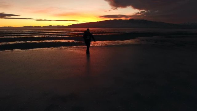 Silhouette of man walking across ice during sunset