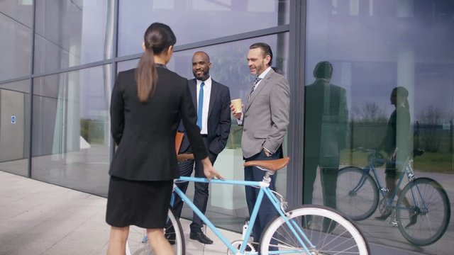  Businesswoman with bicycle leaving office building & talking to coworkers