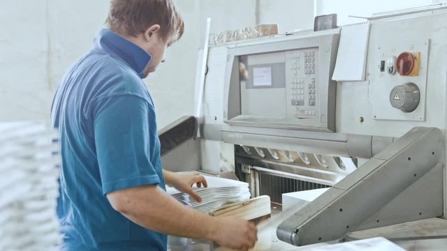 Man works with cutter guillotine machine at printing factory - typography