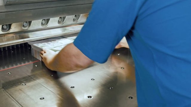 Manual labour at printing factory - man's hands and industrial cutter for cutting paper shears - guillotine machine - close up