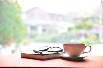 Coffee cup with book, pen and glasses on a wooden table