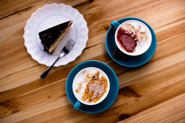 Two cups of coffee with cinnamon are on the table with a piece of chocolate cake