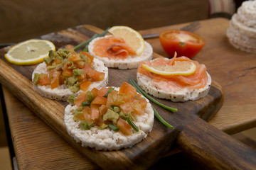 Snacks from rice cookies, salmon, tomatoes, avocado on cutting board and wooden table.