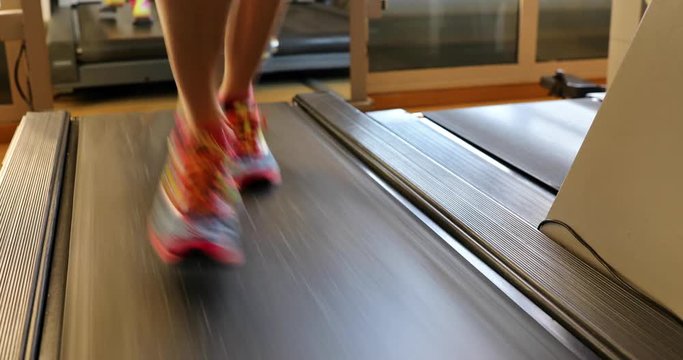 Fitness model woman running on treadmill with muscular legs indoor. Colorful gym shoes of girl on gym tapis roulant. Fast training indoor. Healthy active lifestyle . 4K front close up view.