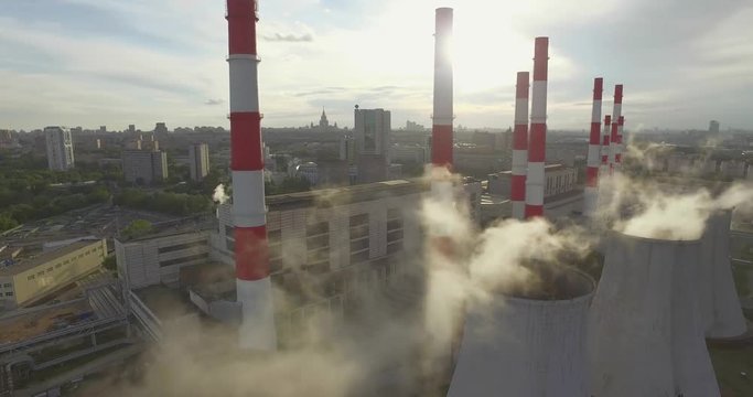 Aerial 4K shot of smoke or steam coming from an industrial chimney, Thermal power plant with huge cooling towers in city suburbs. Industry scenery, factory view, pollution and global warming concept