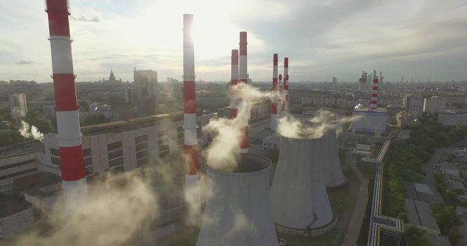 Aerial 4K shot of smoke or steam coming from an industrial chimney, Thermal power plant with huge cooling towers in city suburbs. Industry scenery, factory view, pollution and global warming concept