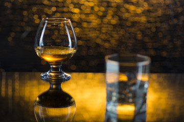 Glass o whisky with ice and wineglass of coghac on yellow bokeh background