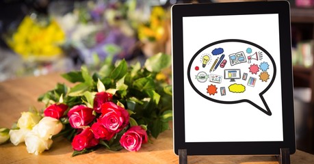 Various icons on digital tablet by flowers on table