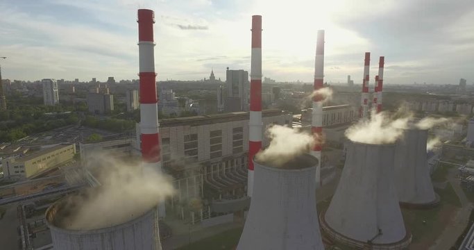 Aerial 4K shot of smoke or steam coming from an industrial chimney, Thermal power plant with huge cooling towers in city suburbs. Industry scenery, factory view, pollution and global warming concept