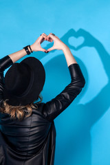 Fashion hipster woman posing on blue background. Black hat, leather jacket, blond curly hair, bright red lips, sunglasses.Trendy fashion summer style.