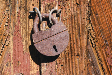 Old rusty lock on wooden doors with cracks, close-up view.
