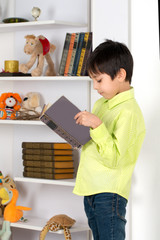 schoolboy stands at the book shelf and reads the book