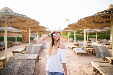 Fototapeta premium Woman walking on a tropical beach holiday. Luxury wooden lounge and sunny outdoors background