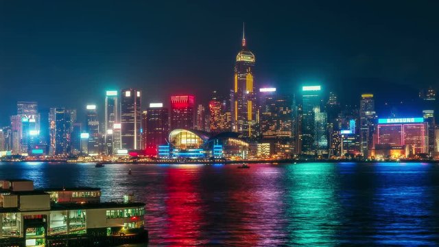 Scenic view over Hong-Kong skyscrapers at night. Nighttime skyline of Victoria harbor with fast moving boats and colorful water reflections. 4K time lapse.