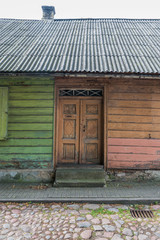 Fragment of brown and green vintage old wooden wall with door and tiled roof. Textural background. Daugavpils, Latvia.