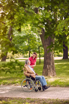 elderly man in wheelchair talking with daughter in the park- happy family time.