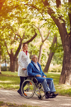 Nurse pushing senior man in wheelchair.