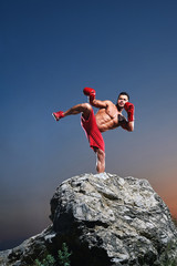 Young male boxer with strong ripped muscular body training outdoors kickboxing boxing fighting...