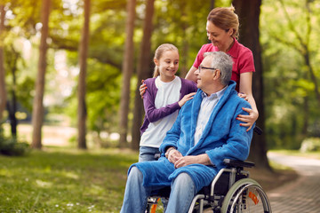 woman visiting her disabled father in wheelchair with granddaughter and enjoying time together.