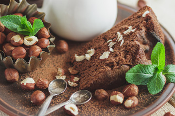 Piece of chocolate cake, mint leaves, hazelnuts, and jar with milk