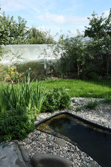 Rural landscape garden with a preformed plastic pond, rockery, lawn and flower bed in the sunny day