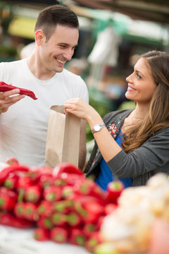 Couple choosing red pepper in grocery store.