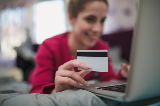 Beautiful woman holding credit card and shopping online in bedroom alone