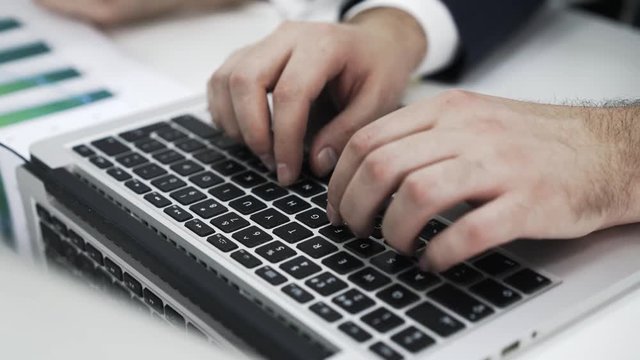 Close up of man hands typing at a laptop keyboard while his boss is pointing at the screen and making suggestions. Locked down real time close up shot