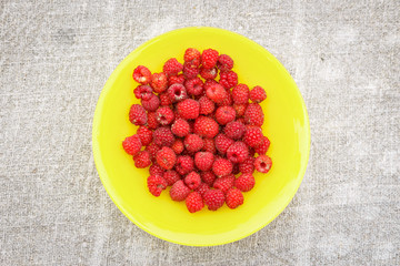 a heap of ripe raspberries on the yellow round plate