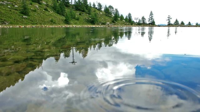 Rain and sky reflection in alpin lake.mov / Some drops of rain are falling in a beautiful alpine lake in dolomiti region, italy, in an inusual point of view
