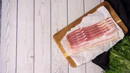 Fresh raw cold sliced bacon with fresh salad on the wood background