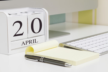 Cube shape calendar for April 20 and computer with white screen on table. 