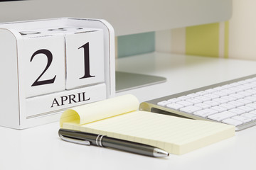 Cube shape calendar for April 21 and computer with white screen on table. 