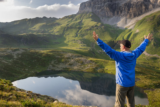 Hiker standing with raised hands near the beautiful mountain lake at sunset