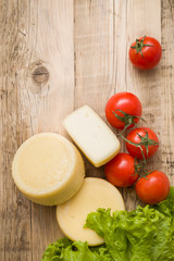 Top view on cut cheese heads on wooden board served with tomatoes and fresh salad. Serving French homemade cheese. Food concept